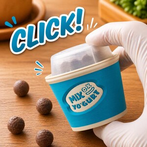 May include: A blue and white yogurt cup with the text "MIX OX YOGURT" is held by a gloved hand. The word "CLICK!" is written above the cup. Several small, round, brown food items are scattered on a wooden surface.
