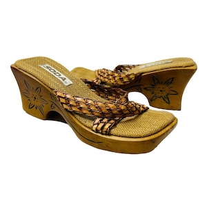 May include: A pair of brown woven platform sandals with a wooden wedge heel. The sandals feature a floral design on the heel and the brand name "SODA" is printed on the footbed.