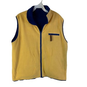 May include: A reversible yellow fleece vest with a navy blue interior and trim. The vest has a full zipper closure, a stand-up collar, and a small pocket with a brown accent. The vest is hanging on a white hanger.