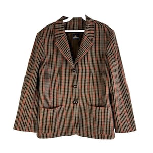 Puede incluir: Una chaqueta de punto marrón y naranja con cierre de botones y dos bolsillos. La chaqueta tiene un estilo clásico y está hecha de una tela suave y cómoda.