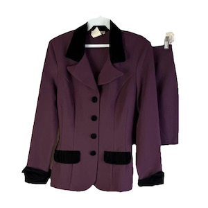 May include: A two-piece purple suit with a black velvet collar, pocket trim, and cuffs. The blazer has four black buttons and a tailored fit. The skirt is a matching solid purple color.