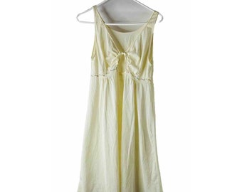 May include: A pale yellow sleeveless dress with a tie detail at the back and a floral embroidered trim around the neckline.