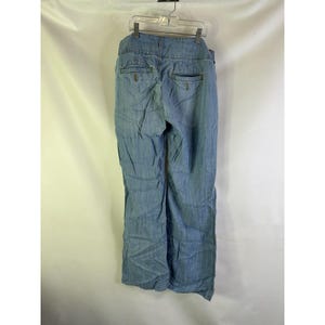 May include: Light blue denim pants with a high waist and wide leg design. The pants have two back pockets and are hanging on a clear plastic hanger. The fabric appears to be slightly wrinkled.