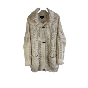 May include: A cream-colored cable knit cardigan with a button closure and two pockets. The cardigan has a wide collar and long sleeves.