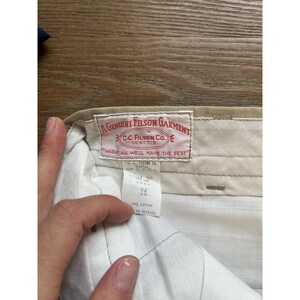 May include: A pair of beige trousers with a white label that reads "A Genuine Filson Garment C-C-Filson Co. Seattle Might as well have the best" and a smaller white label that reads "Style 55 Size 36 100% Cotton See Reverse."