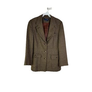 Può includere: Un blazer marrone e nero a fantasia pied-de-poule, con revers a lancia, due tasche anteriori e tre bottoni. Il blazer è appeso a una gruccia bianca su sfondo bianco. La fodera interna è di colore marrone pieno.