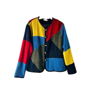 May include: A patchwork jacket in a vibrant colour scheme. The jacket has a V-neck and long sleeves, with a geometric design featuring red, yellow, blue, green, and black panels. It fastens with buttons and has a black trim.