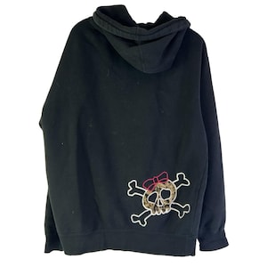 May include: Black hooded sweatshirt with a skull and crossbones design on the back. The skull has a leopard print pattern and a pink bow. The sweatshirt has a drawstring hood.