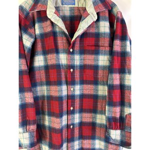 May include: A long-sleeved plaid shirt in red, blue, and white. The shirt has a button-down front, a collar, and a chest pocket. The fabric appears to be a soft, woven material.