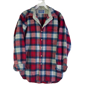 May include: A red, blue, and white plaid button-down shirt hanging on a white hanger. The shirt has a collared neckline and a chest pocket. The shirt is made of a thick, warm material, perfect for cooler weather.