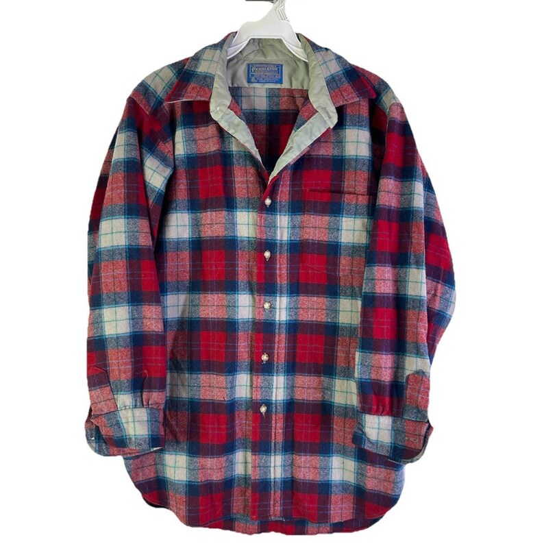 May include: A red, blue, and white plaid button-down shirt hanging on a white hanger. The shirt has a collared neckline and a chest pocket. The shirt is made of a thick, warm material, perfect for cooler weather.