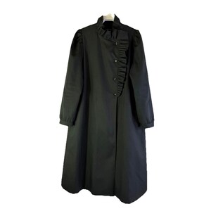 May include: Black long coat with a high ruffled collar and button closure. The coat features long sleeves and a ruffled accent down the front. The coat is a solid black color.