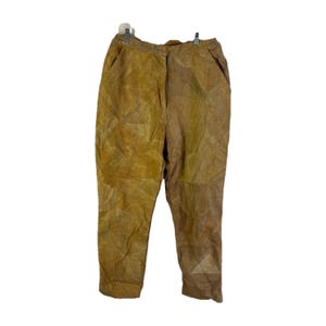 以下が含まれることがあります： パッチワークデザインのベージュ色のパンツ。 パンツにはボタンとジッパーの留め具、ポケット、ストレートレッグが付いています。 生地はスエードまたは同様の素材のようです。 パンツは白い背景にハンガーに吊るされています。