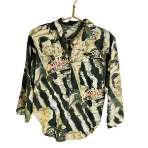 May include: A long-sleeved button-up shirt with a colorful print featuring a zebra pattern, palm trees, and the text "Casablanca Claude".