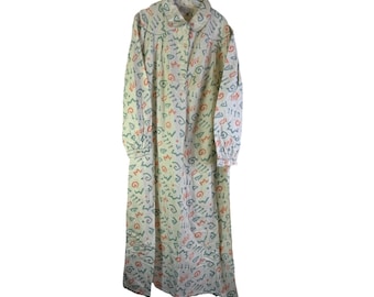 Puede incluir: Camisón largo blanco con cuello y mangas largas. El camisón está cubierto con un patrón de formas rojas, azules y verdes. La prenda está colgada de una percha sobre un fondo blanco.