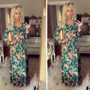 May include: A woman wearing a long-sleeved green dress with a floral pattern. The dress has a V-neckline and a ruffled hem. The woman is standing in front of a mirror and is holding a phone in her hand.