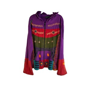 Op de afbeelding: Een paarse hoodie met een rits en een kleurrijk patchwork-ontwerp met geborduurde bloemen en sterren. De hoodie heeft een losse pasvorm en lange mouwen.
