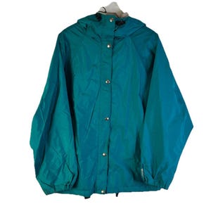 Puede incluir: Chaqueta con capucha de color turquesa con cierre de botones. La chaqueta tiene una capucha con cordón y puños elásticos. Está hecha de un material ligero y resistente al agua. Talla mediana.
