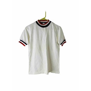 Puede incluir: Camiseta blanca de manga corta con cuello alto y ribetes rojo, blanco y azul alrededor del cuello y las mangas.