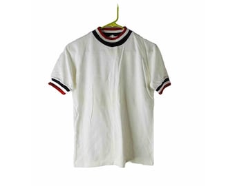 Può includere: Maglietta bianca a maniche corte con collo alto e bordini rosso, bianco e blu intorno al collo e alle maniche.