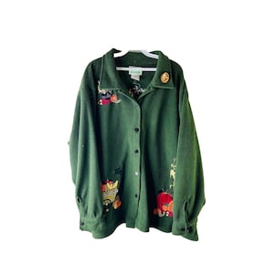 Könnte beinhalten: Ein grünes Fleece-Hemd mit Knöpfen und gestickten Herbstmotiven. Das Hemd hat einen Knopfleisten vorne und lange Ärmel.