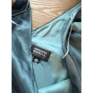 May include: Close-up of a teal-colored dress with a V-neckline. The dress has a satin-like sheen and a label that reads "Adrianna Papell."