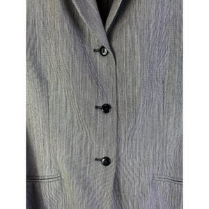 Puede incluir: Primer plano de un blazer gris con tres botones negros. El blazer tiene una tela texturizada y solapas con muescas. Los botones son redondos y brillantes, contrastando con la tela mate.