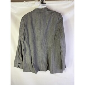 Puede incluir: Un blazer gris con un sutil patr&oacute;n de rayas verticales. El blazer tiene solapas con muescas, tres botones en cada pu&ntilde;o y un cierre de dos botones. La parte trasera del blazer es visible, mostrando el ajuste y la construcci&oacute;n.