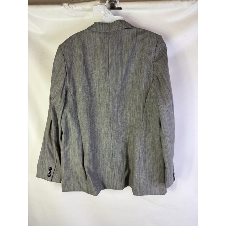 Puede incluir: Un blazer gris con un sutil patr&oacute;n de rayas verticales. El blazer tiene solapas con muescas, tres botones en cada pu&ntilde;o y un cierre de dos botones. La parte trasera del blazer es visible, mostrando el ajuste y la construcci&oacute;n.