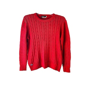 May include: A red cable knit sweater with a small crocodile logo on the left side.