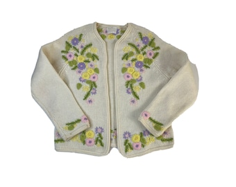 May include: A white knitted cardigan with floral embroidery in shades of yellow, purple, and green.