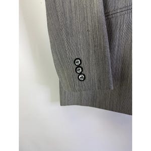 Puede incluir: Primer plano de una manga de blazer gris con tres botones negros. La tela tiene un sutil patr&oacute;n de rayas verticales. El blazer es de color neutro, adecuado para varios conjuntos.