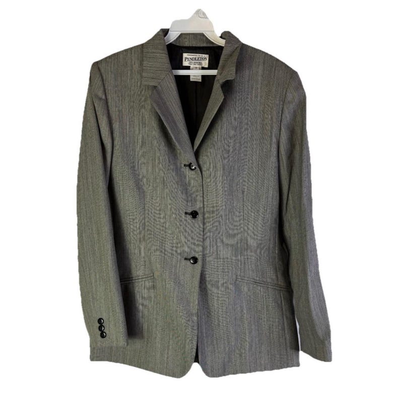 Puede incluir: Un blazer gris con un sutil patr&oacute;n de rayas verticales, con solapas y tres botones negros en la parte delantera. El blazer tiene mangas largas con tres botones en cada pu&ntilde;o. La marca "Pendleton" es visible.