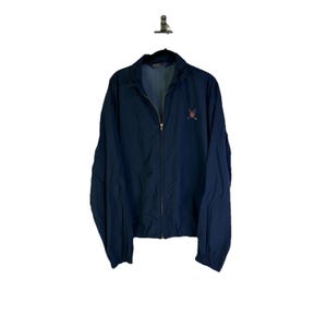 Puede incluir: Chaqueta azul marino con cremallera y un pequeño logotipo bordado en el pecho. La chaqueta tiene cuello alto y cremallera completa. Fabricada con un material ligero, es adecuada para usar en capas.