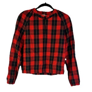 May include: A red and black plaid long-sleeve shirt. The shirt is hanging on a black hanger. The plaid pattern is a classic design, with a grid of black lines over a red background. The shirt has a round neckline and long sleeves.