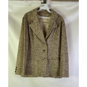 May include: A tan tweed blazer with a notched collar, two front pockets, and gold-colored buttons. The blazer is hanging on a white hanger against a white background. The jacket has a classic, tailored design.