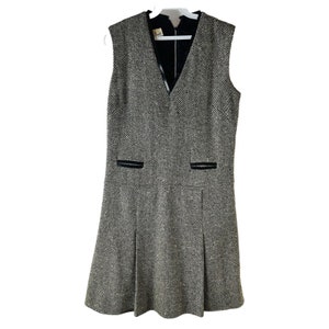 May include: A sleeveless black and white herringbone dress with a V-neckline and black trim. The dress has pockets on the front and a pleated skirt.