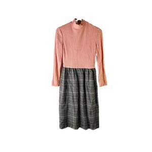 May include: A pink and black dress with a turtleneck and a plaid skirt.