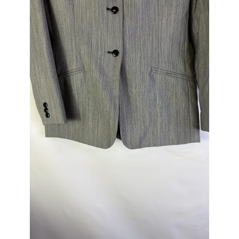 Puede incluir: Un blazer gris con un patr&oacute;n de rayas verticales texturizadas. El blazer tiene dos botones negros, un bolsillo y tres botones en la manga. La chaqueta es de estilo cl&aacute;sico.