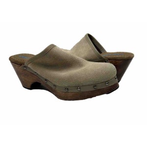 May include: A pair of beige suede clogs with wooden heels and metal accents. The clogs have a wedge heel and a rounded toe.