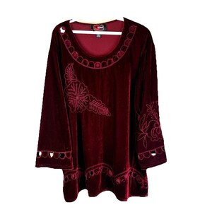May include: A burgundy velvet top with long sleeves and a scoop neckline. The top features embroidered floral designs on the front and sleeves, with decorative cutouts on the sleeves. The Arrow brand tag is visible.