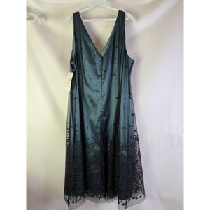 May include: A teal-colored formal dress with a V-neck and sleeveless design. The dress features a satin bodice and a sheer overlay skirt with black floral embroidery. The dress is hanging on a white hanger.
