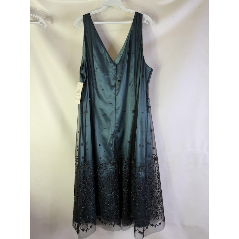 May include: A teal-colored formal dress with a V-neck and sleeveless design. The dress features a satin bodice and a sheer overlay skirt with black floral embroidery. The dress is hanging on a white hanger.