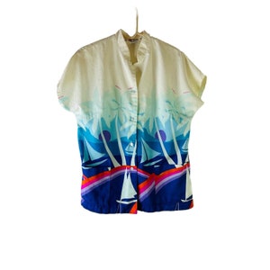 Könnte beinhalten: Ein kurzärmeliges, cremefarbenes Hemd mit Knöpfen und einem tropischen Druck in Blau, Orange und Pink mit Palmen und Segelbooten.