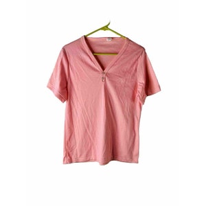 May include: A pink short-sleeved t-shirt with a v-neck and a button closure at the neckline.