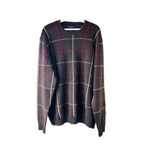 Könnte beinhalten: Ein brauner Pullover mit einem karierten Muster in Rot, Weiß und Beige. Der Pullover hat einen Rundhalsausschnitt und lange Ärmel. Der Markenname "Rustic Blend" ist auf dem Etikett sichtbar.