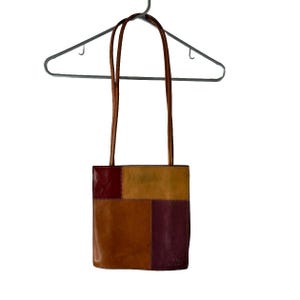 May include: A brown leather tote bag with a patchwork design in shades of brown, red, and yellow. The bag has a single strap and a small label that reads "Duluth Trading Co."