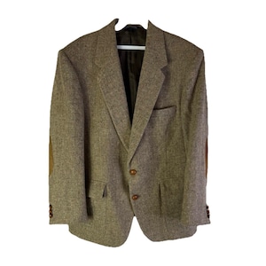 Könnte beinhalten: Braune Tweed-Blazer mit Ellbogenpatches und einem Zwei-Knopf-Verschluss. Der Blazer hat ein fallendes Revers, zwei Vordertaschen und drei Knöpfe an jeder Manschette. Das Innenfutter ist dunkelbraun.