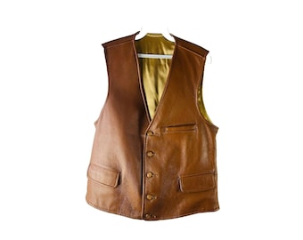 May include: A brown leather vest with a button-up front and two pockets. The vest has a gold satin lining.