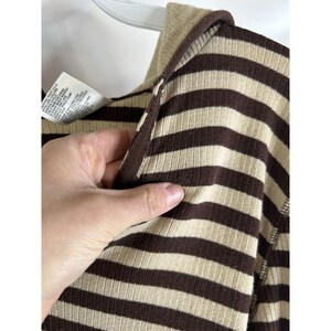 Op de afbeelding: Close-up van een gestreept hooded shirt in bruin en beige met een rits. Het shirt is gemaakt van een zachte, geribbelde stof.